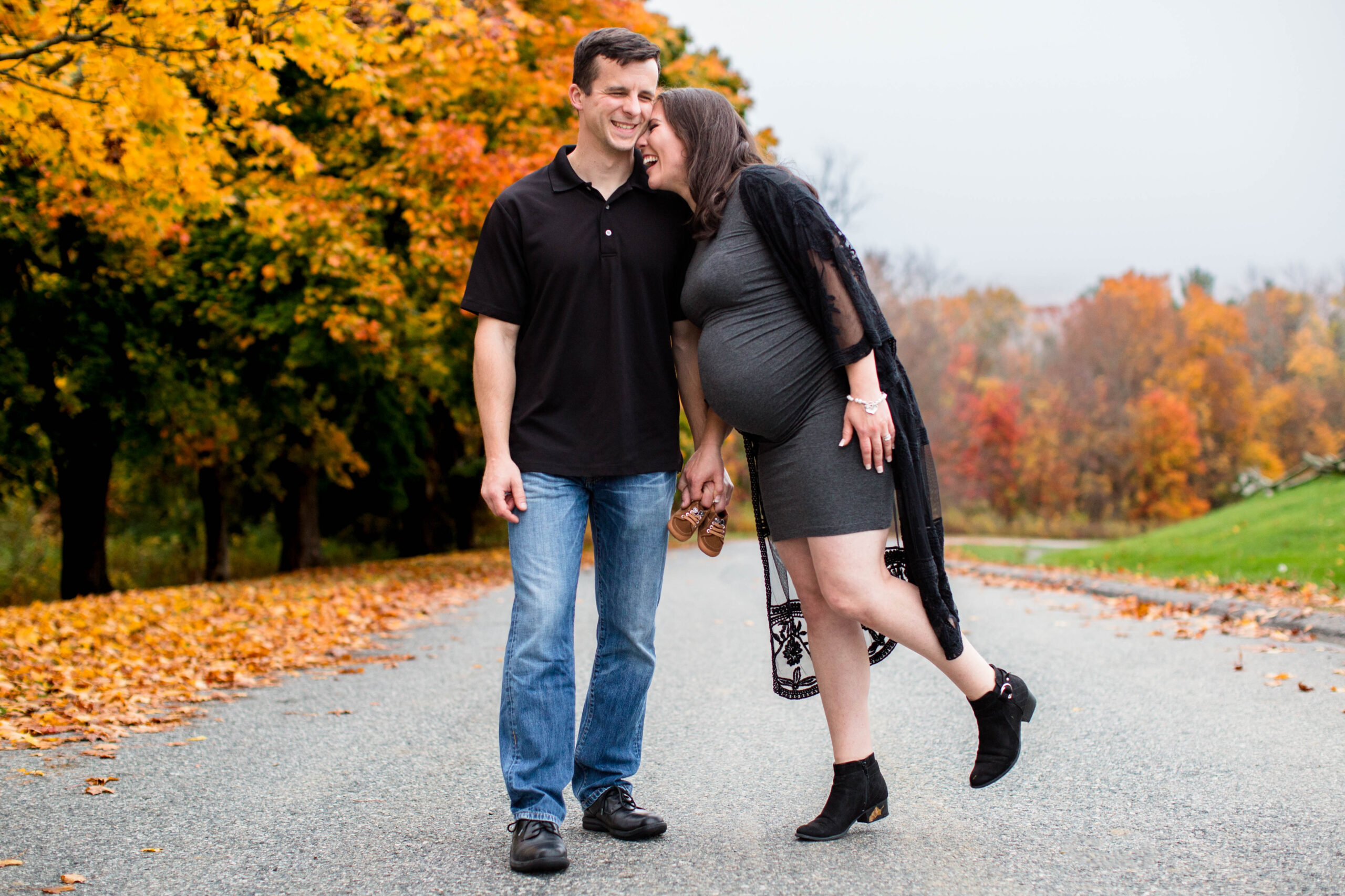 Pregnant women laughing and snuggling into her husband in beautiful fall weather